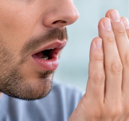 Nahaufnahme eines Mannes, der bei Mundtrockenheit die Hand vor seinen geöffneten Mund hält.